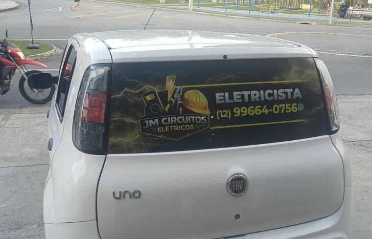 Carro da JM com o logo, a palavra Eletricista e o telefone (12) 99664-0756 no vidro traseiro